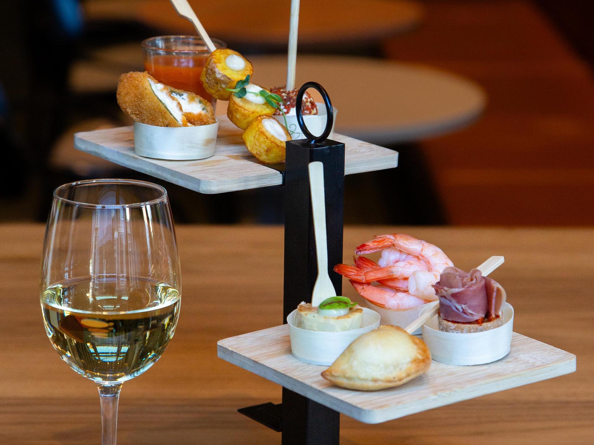Glas witte wijn met tapas hapjes op een etagère