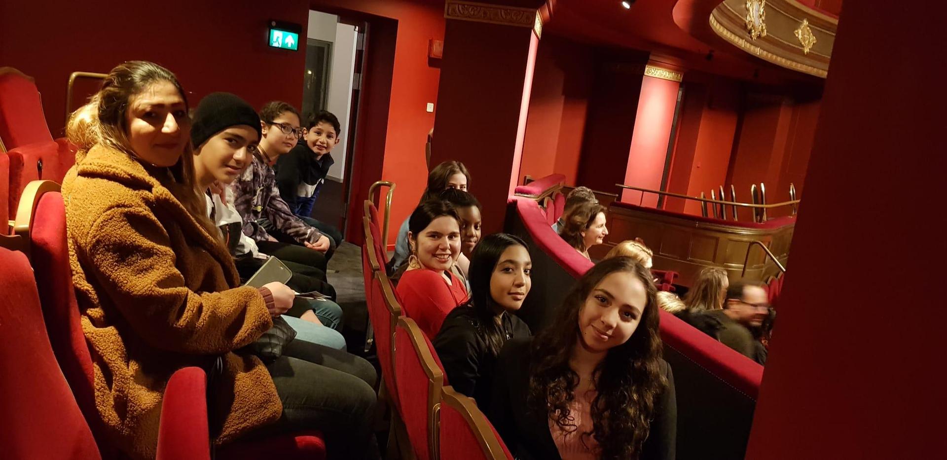 Groep kinderen met begeleider in de rode stoelen van de Stadsschouwburg.